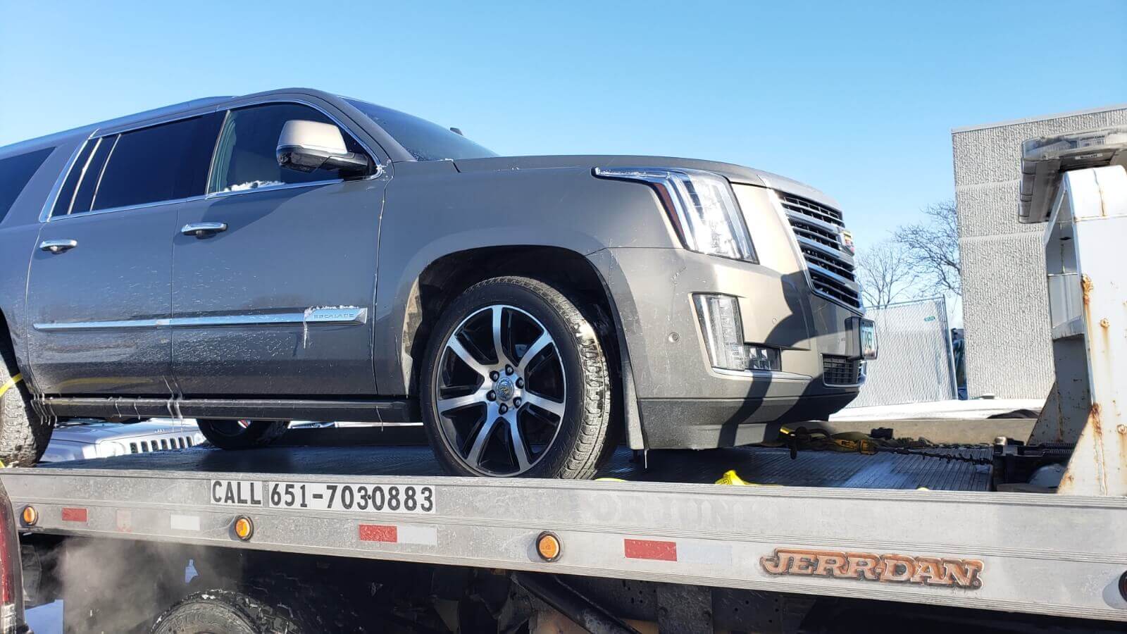 Tow truck driver changing a flat tire on the roadside.