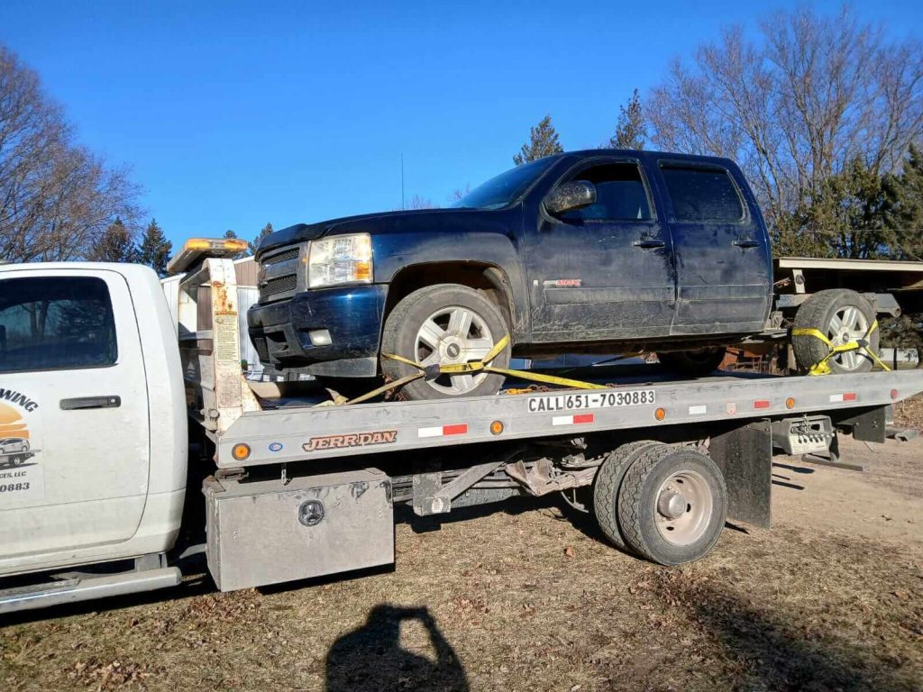 Tow truck transporting a broken-down car on a city road.